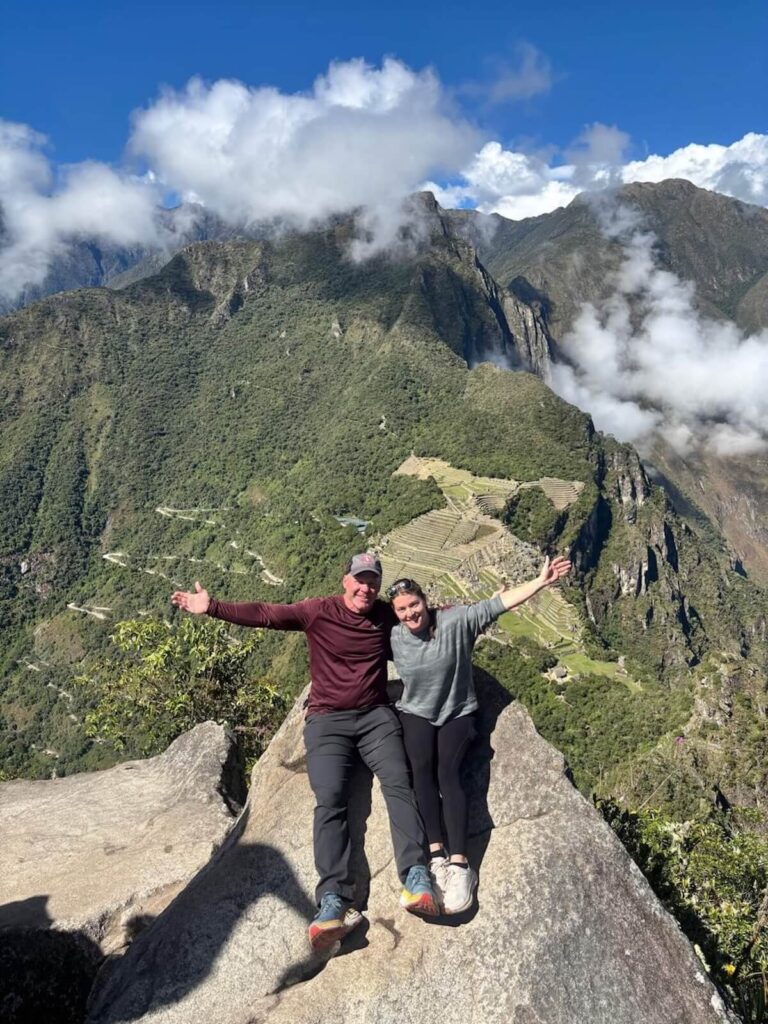 Travelers at Machu Picchu classic viewpoint with Huayna Picchu and dramatic cloud formations in Peru