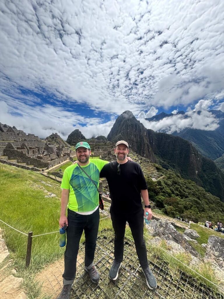 Travelers at Machu Picchu classic viewpoint with Huayna Picchu and dramatic cloud formations in Peru