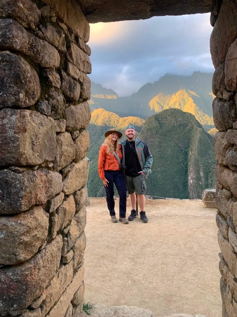 Couple framed by an Inca stone doorway with mountain views at Machu Picchu, Cusco, Peru